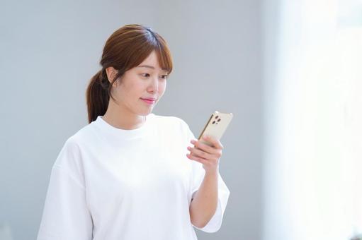 窓際でスマホを見る女性 女性,スマートフォン,持つの写真素材