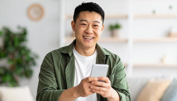 笑顔でスマホを見る男性の室内ポートレート 笑顔でスマホを見る男性の室内ポートレートの写真