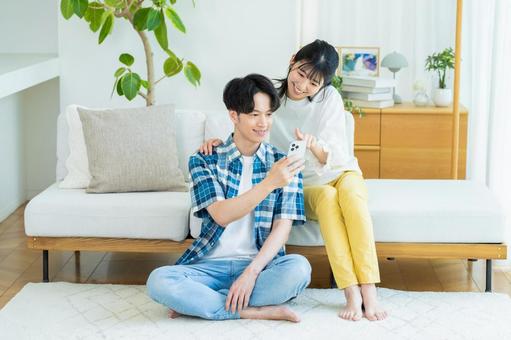 リビングでスマホを見るカップル スマホ,笑顔,カップルの写真素材