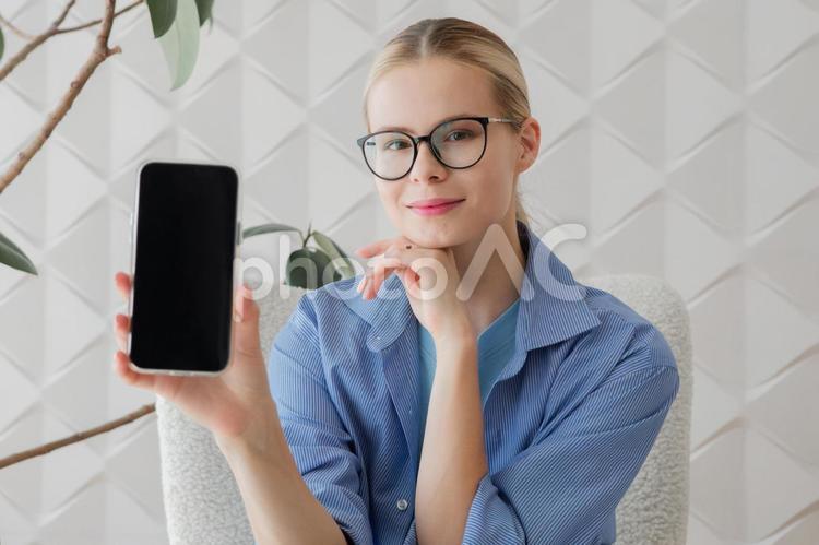 カメラ目線でスマホ画面を見せる女性 女性,スマートフォン,画面の写真素材