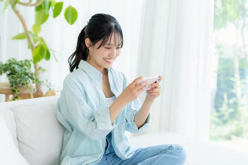 部屋でスマホを操作する若い女性 スマホ,笑顔,女性の写真素材