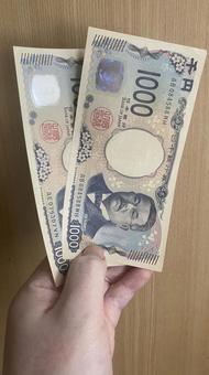 千円札を2枚持っている手 千円札を2枚持っている手の写真