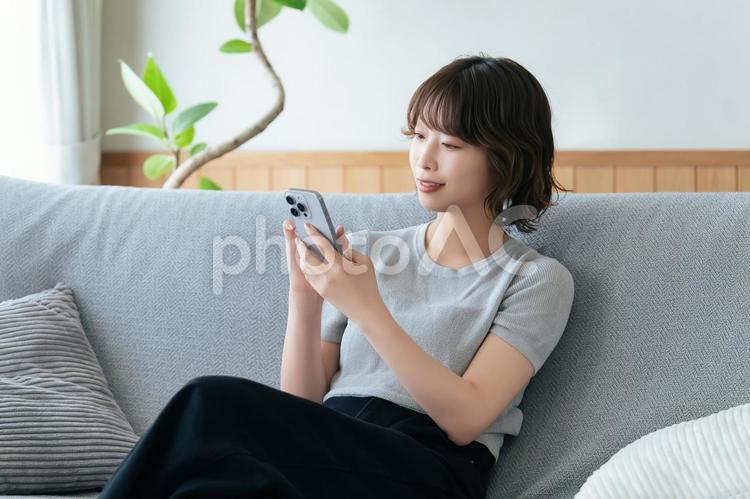 ソファに座ってスマホを使う笑顔の女性 女性,スマホ,スマートフォンの写真素材