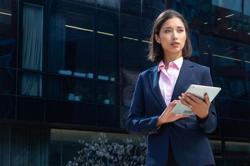オフィスビルの外でタブレットを持って立つアジア人ビジネスウーマン ビジネスウーマン,ビジネス,女性の写真素材