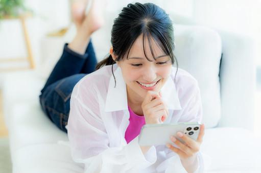 部屋でスマホを操作する若い女性 部屋でスマホを操作する若い女性 スマホ,若い女性,笑顔の写真素材