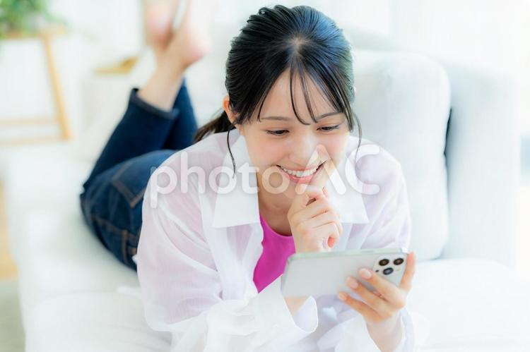 部屋でスマホを操作する若い女性 スマホ,若い女性,笑顔の写真素材