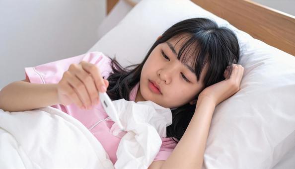 発熱して寝込んで体温計を見る女の子 発熱して寝込んで体温計を見る女の子の写真