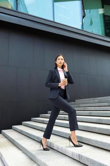 オフィスビルの外の階段でコーヒー片手に電話する女性 ビジネスウーマン,ビジネス,女性の写真素材