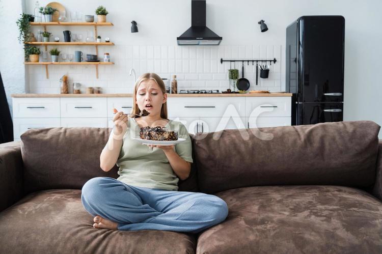 ソファーに座って苦しそうにケーキを食べる女性 女性,人物,見るの写真素材