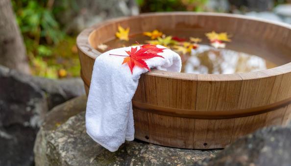 紅葉した落葉が舞い落ちる露天風呂の風呂桶 紅葉した落葉が舞い落ちる露天風呂の風呂桶の写真