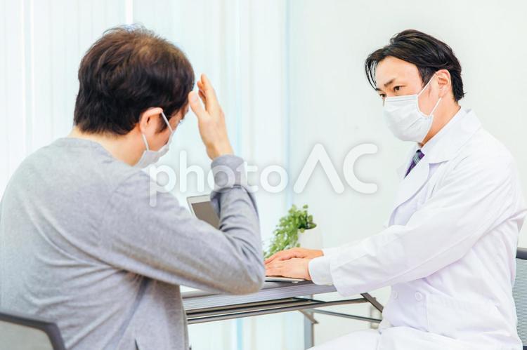 パソコンで診察するマスク姿の男性医師（頭痛） 認知症,痴呆症,脳ドックの写真素材