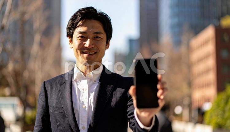 携帯画面を見せて笑うビジネスマン スマートフォン,都市,高層ビルの写真素材