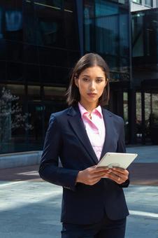 オフィスビルの外でタブレットを持って立っているカメラ目線のアジア人女性 ビジネスウーマン,ビジネス,女性の写真素材