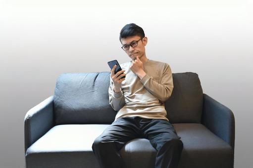 ソファーでスマホを見る男性 ソファーでスマホを見る男性 スマホ,悩む,調べるの写真素材