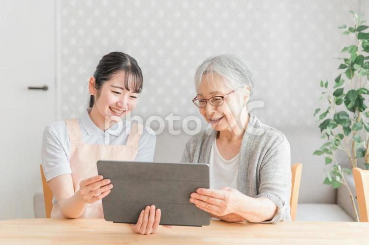 タブレットを使うエプロン姿の女性と高齢者女性 高齢者,介護士,タブレットの写真素材