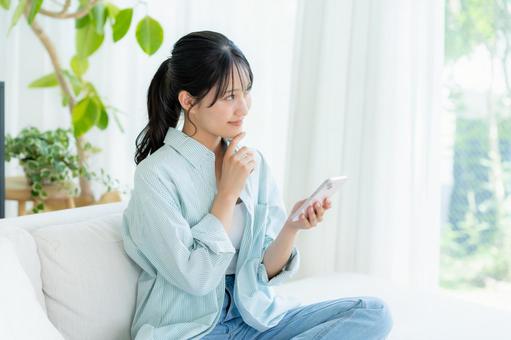 部屋でスマホを操作する若い女性 スマホ,笑顔,女性の写真素材