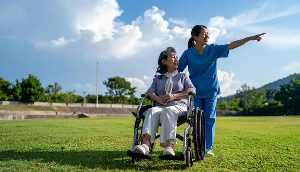 青空の下　同方向を見るシニア女性と介護士の写真