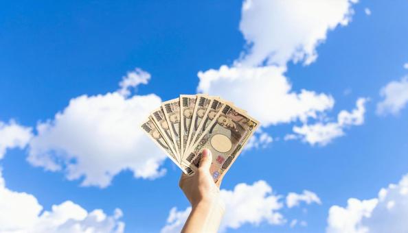 一万円を持つ手　青空背景の写真