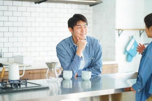 キッチンで向かい合って頬杖をつく男性 キッチンで向かい合って頬杖をつく男性の写真