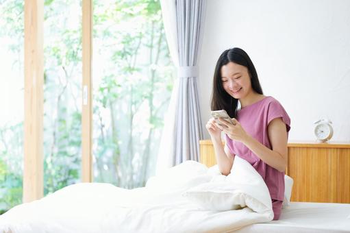 嬉しそうにベッドでスマホを見ている日本人女性 女性,スマートフォン,持つの写真素材