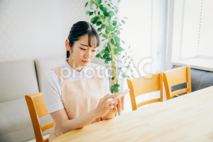 スマホを使うエプロン姿の女性（困る） スマホ,介護士,スマートフォンの写真素材