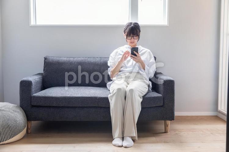 ソファーでスマホを操作する女性　 スマホ,リラックス,女性の写真素材