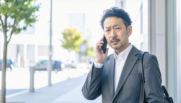 困った表情で電話する中年 困った表情で電話する中年の写真
