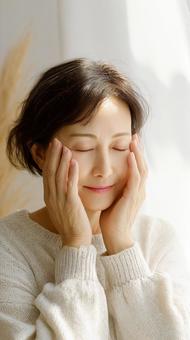 目を閉じ、顔に手を添える穏やかな中年女性 目を閉じ、顔に手を添える穏やかな中年女性の写真