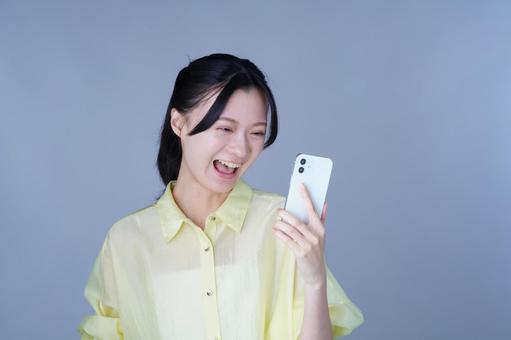 スマホをもって笑顔の黄色い服を着た女性 女性,スマートフォン,持つの写真素材