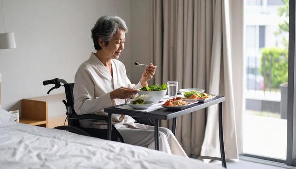 病室で車いすに座り食事をする高齢女性患者の写真