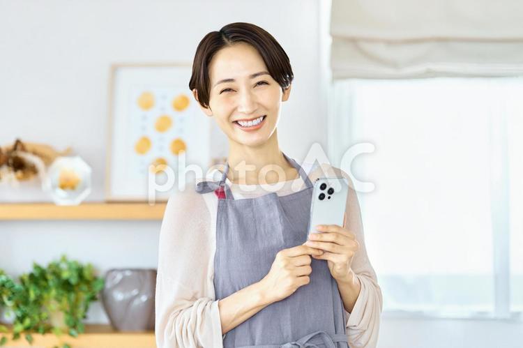 スマートフォンを持つ主婦　リビングルーム スマホ,主婦,エプロンの写真素材