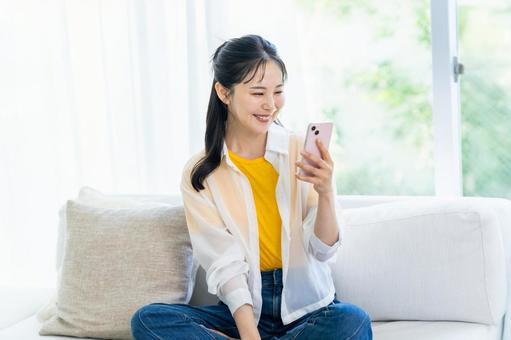部屋でスマホを操作する女性 スマホ,笑顔,部屋の写真素材