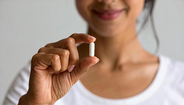 薬一錠を親指と人差し指で持つ女性 薬一錠を親指と人差し指で持つ女性の写真