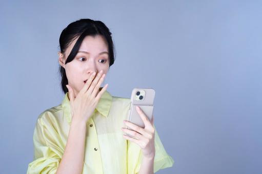 スマホを見て驚いている黄色い服の女性 女性,スマートフォン,持つの写真素材