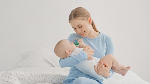 玩具を口に入れる赤ちゃんを見つめる笑顔の女性 玩具を口に入れる赤ちゃんを見つめる笑顔の女性 親子,抱っこ,見つめるの写真素材