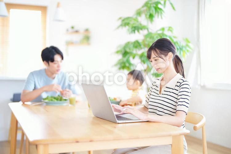 真顔でパソコンをする女性と食事中の父子 女性,ノートパソコン,仕事の写真素材