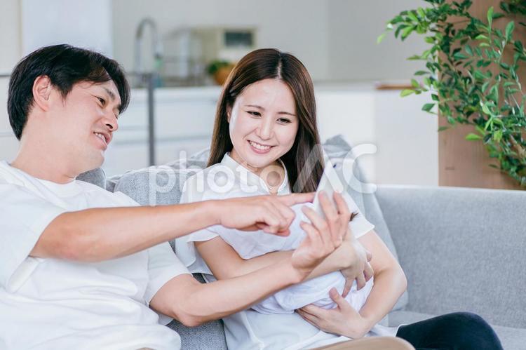 部屋でスマホを使う赤ちゃんを抱く男女 スマホ,夫婦,赤ちゃんの写真素材