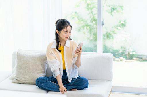 部屋でスマホを操作する女性 スマホ,笑顔,部屋の写真素材