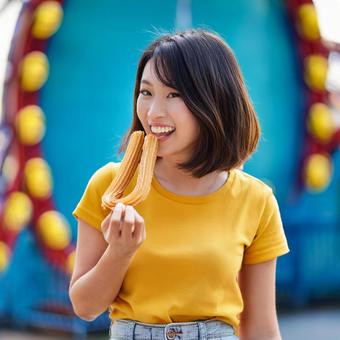 遊園地でチュロスを食べる女性 遊園地でチュロスを食べる女性の写真