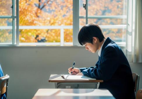 秋の教室で勉強に集中する男子学生の写真