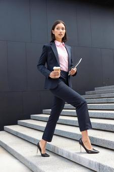 コーヒーとタブレットを持ってオフィスビルの外の階段を登っている女性 ビジネスウーマン,ビジネス,女性の写真素材