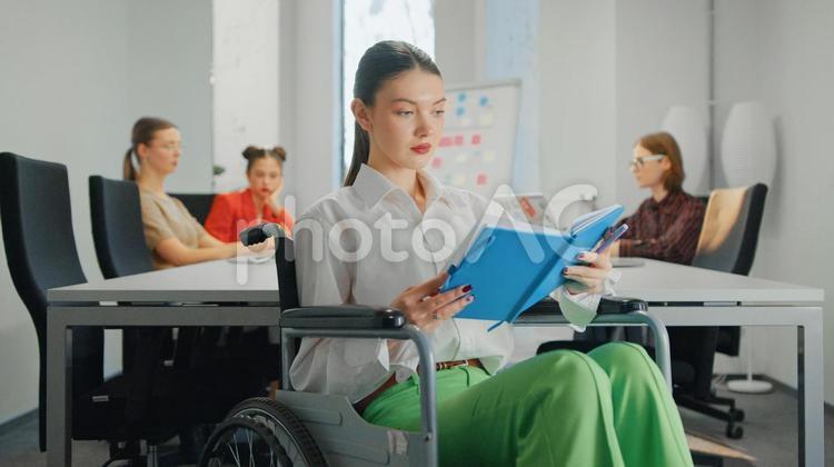 手帳を見る車椅子の女性と同僚たち ビジネス,ビジネスマン,ビジネスウーマンの写真素材