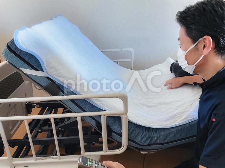 介護ベットを操作する訪問介護士の男性 介護福祉士,福祉,介護士の写真素材