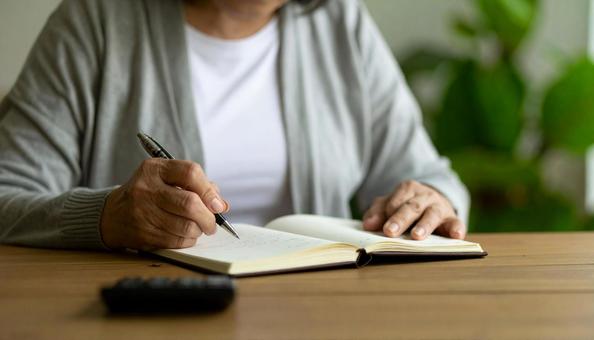 家計簿をつけるシニア女性の手もと 家計簿をつけるシニア女性の手もとの写真