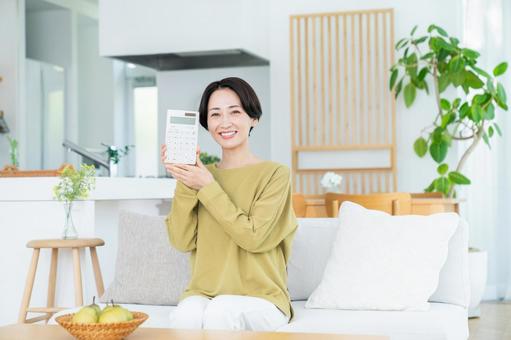 リビングで電卓を持つミドルの女性 リビングで電卓を持つミドルの女性の写真