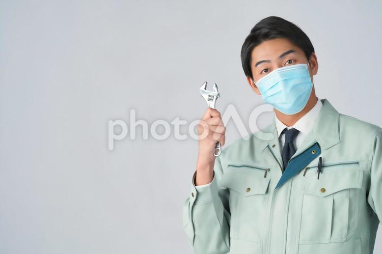 スパナを持っているマスクの男性作業員（白背景） 男性,作業員,カメラ目線の写真素材