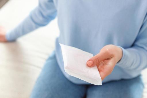 フローリングに座って生理用ナプキンを持っている女性 生理,月経,女性の写真素材