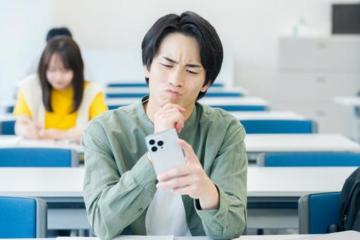 スマホを見ながら悩む大学生 スマホ,大学生,男性の写真素材