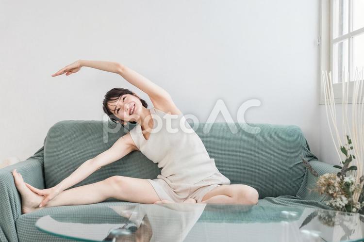ソファで軽くストレッチするアジア人女性 モーニングルーティーン,ストレッチ,柔軟ストレッチの写真素材