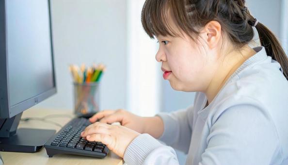 パソコンで作業するダウン症の女性の写真